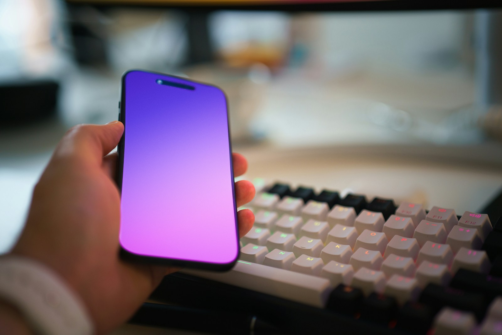 A person holding a cell phone next to a keyboard